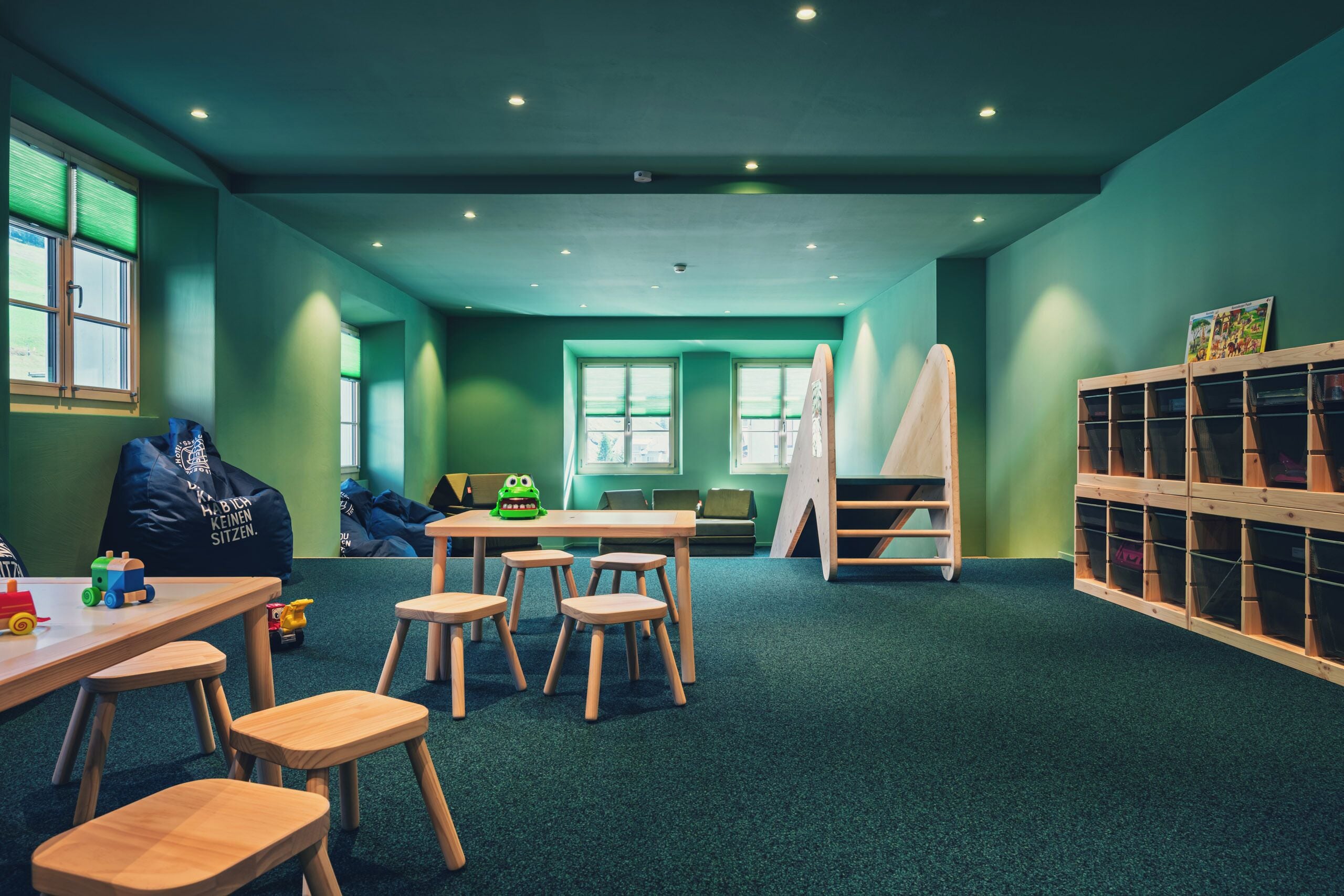 Ein Kinderspielzimmer mit grünen Wänden, Holzmöbeln und Teppichboden.