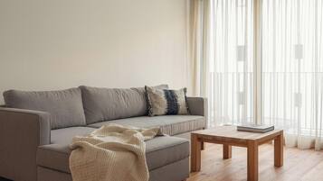 A living room with a grey sofa, a wooden coffee table, and a large window with sheer curtains.