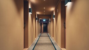 Un couloir d’hôtel avec un sol recouvert de moquette et des portes de chaque côté.