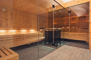 Una sauna con bancos de madera y paredes de vidrio, que cuenta con un calentador central.