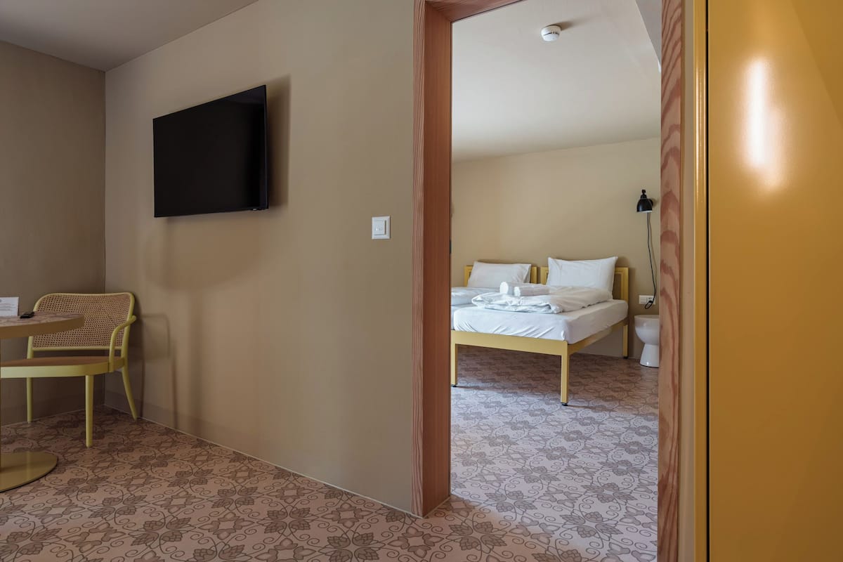A hotel room with a bed, a chair, a table, and a TV mounted on the wall.