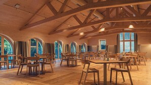 Un vaste hall doté de planchers et de tables en bois, de grandes fenêtres en arc de cercle et d’un haut plafond également en bois.