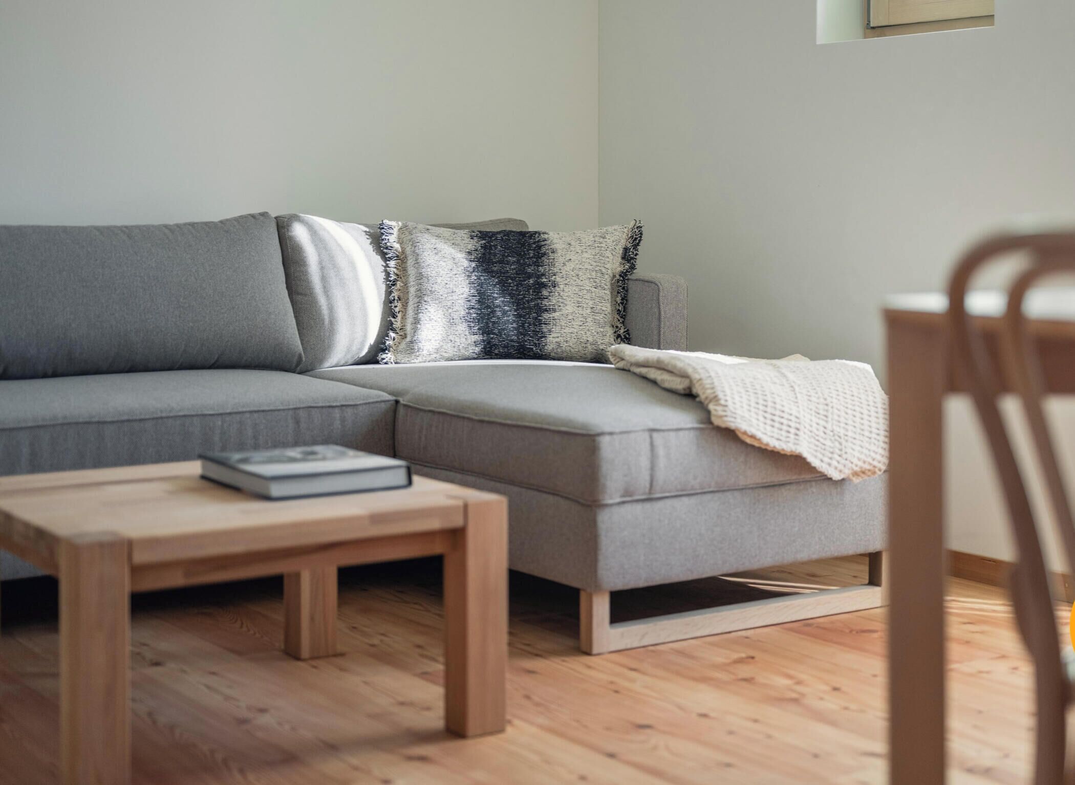 Una sala moderna con un sofá seccional gris, una mesa de centro de madera y una manta blanca.