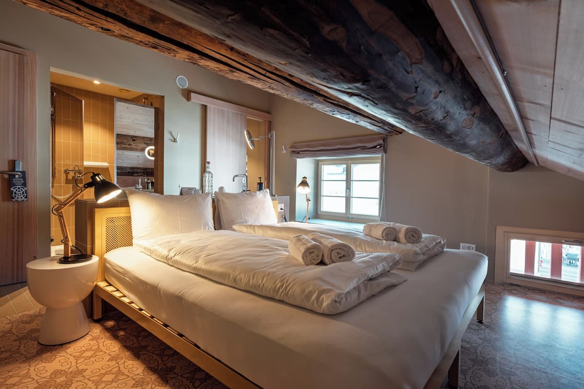 A hotel room with a large bed, bedside lamps, a wooden ceiling, and a window with a view.