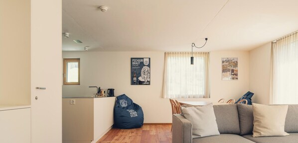 Un salon moderne avec un canapé, un fauteuil poire, un coin repas avec une table et une cuisine en arrière-plan.