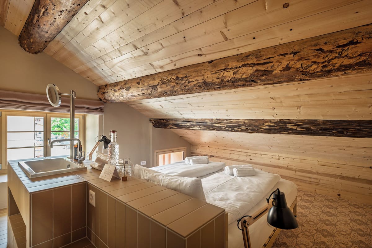 A wooden cabin-style room with a large window, a sink, a mirror, a bedside table, and a lamp.