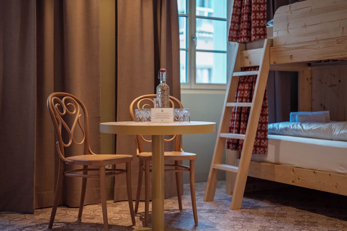 A room with a bunk bed, a round table with chairs, a bottle, and a menu on the table.