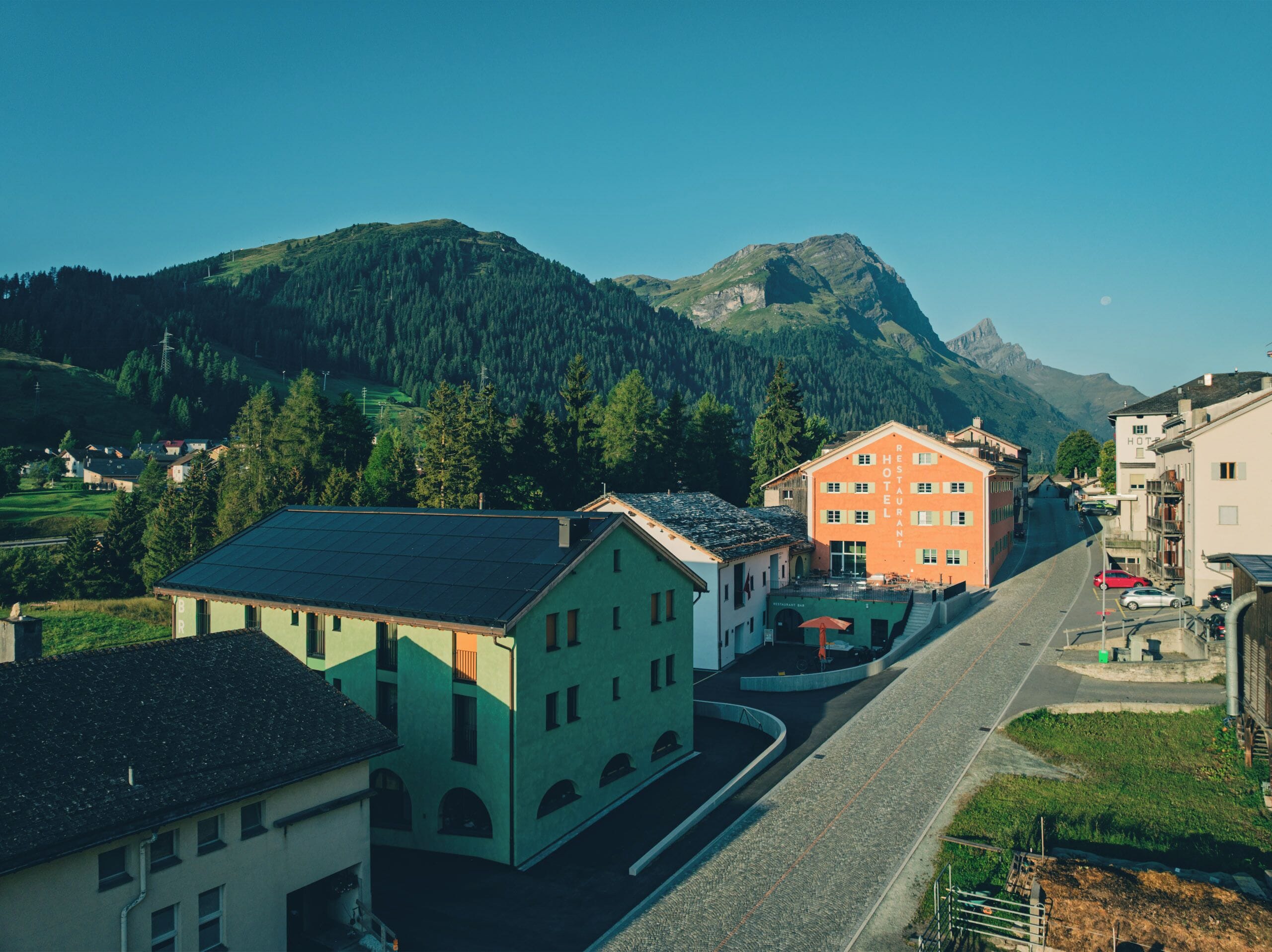 Une rue bordée d’immeubles, dont un restaurant et un hôtel, située dans une région montagneuse.