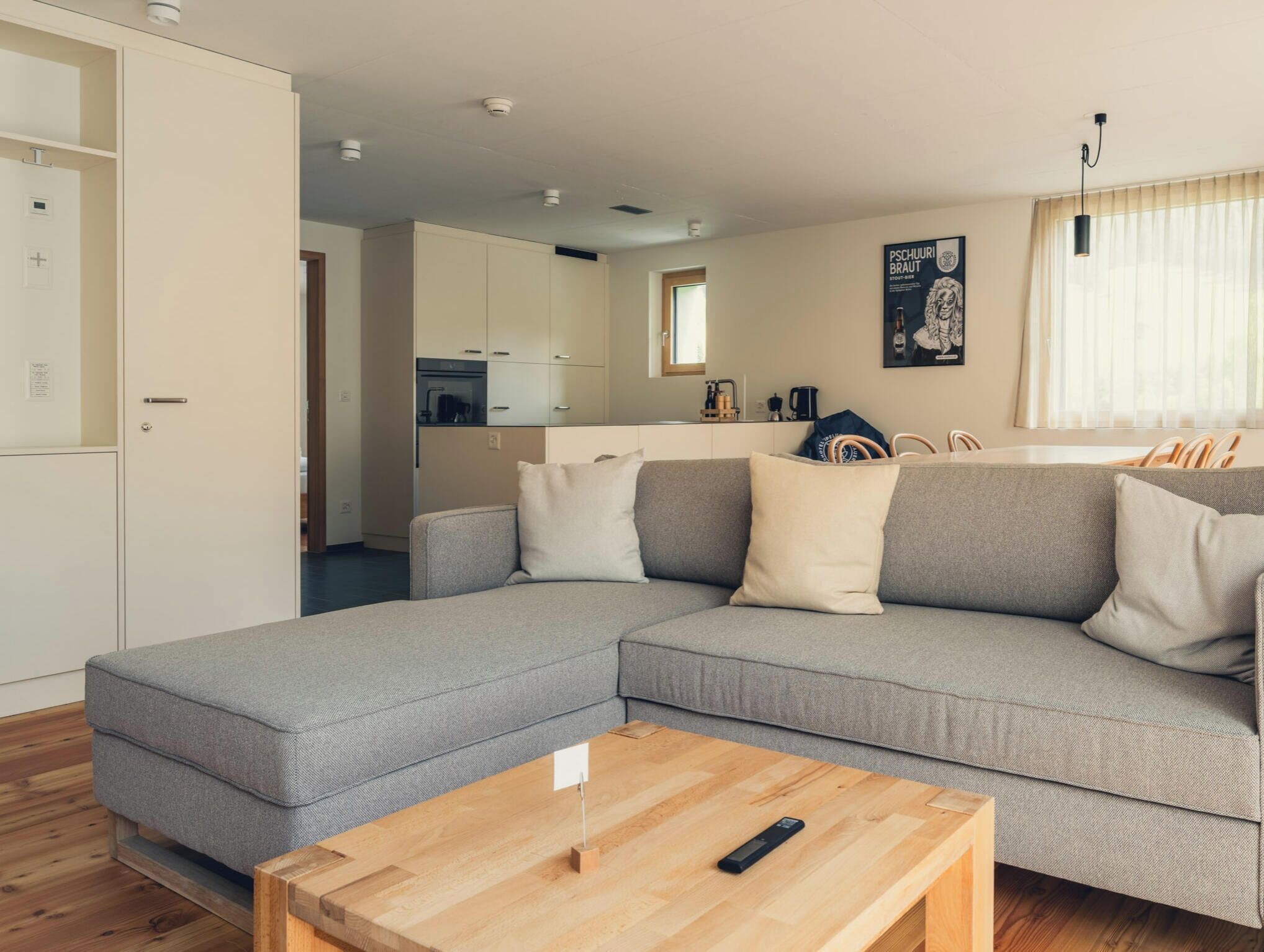 Una sala de estar moderna con un sofá modular gris, una mesa de centro de madera y una cocina al fondo.