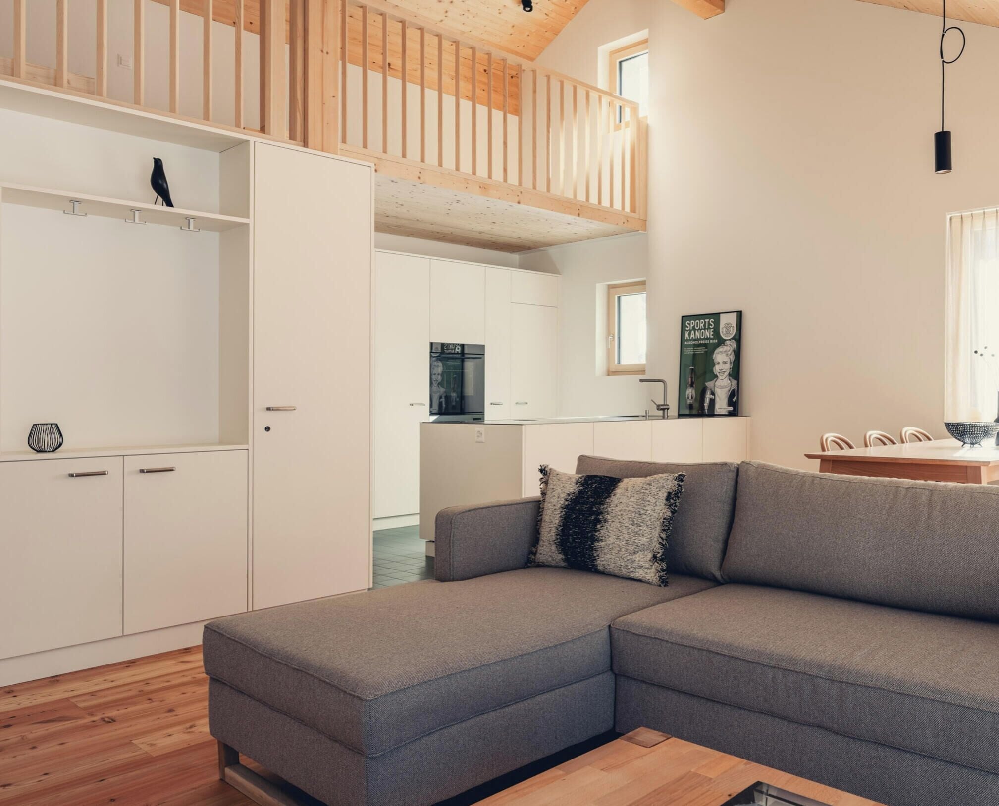 A modern living space with a grey sectional sofa, wooden flooring, and a kitchen in the background.