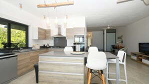 A modern kitchen with a central island, white bar stools, and a dining area with a table and chairs.