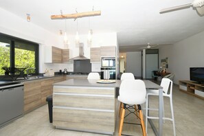 Una cocina moderna con una isla central, taburetes blancos y una zona de comedor con mesa y sillas.