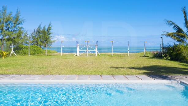 A swimming pool with a view of the ocean and a grassy area with palm trees.