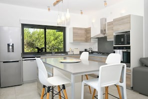 Una cocina moderna con una isla central, sillas blancas, electrodomésticos de acero inoxidable y vistas al exterior.