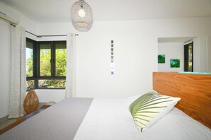 A bedroom with a bed, a wooden headboard, a hanging light fixture, a window with curtains, and a wall with small framed pictures.