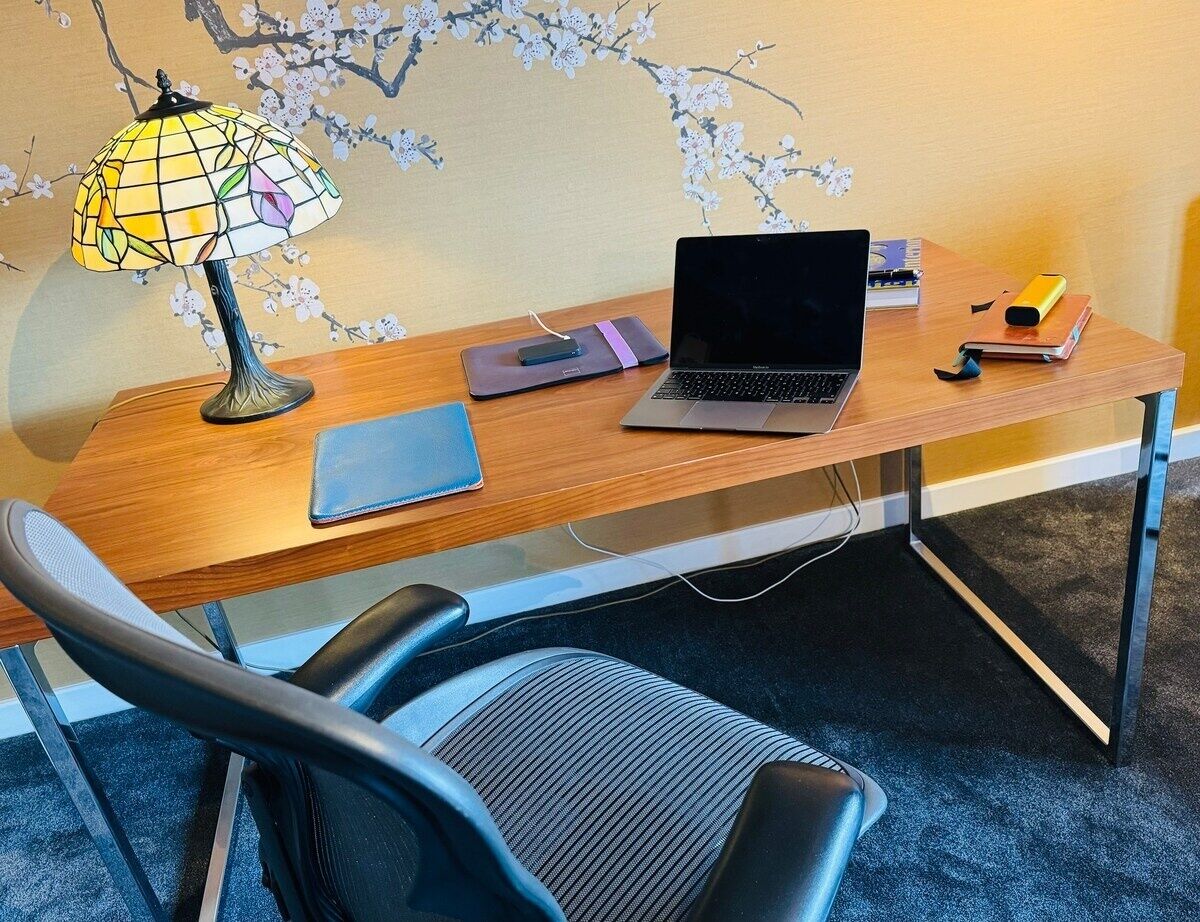 Un bureau en bois avec un ordinateur portable, une lampe et un carnet.