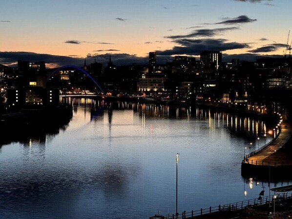 A nighttime cityscape with a river, illuminated buildings, and a bridge. - Stylish Ouseburn Apartment with River & City Views (Tyne and Wear)