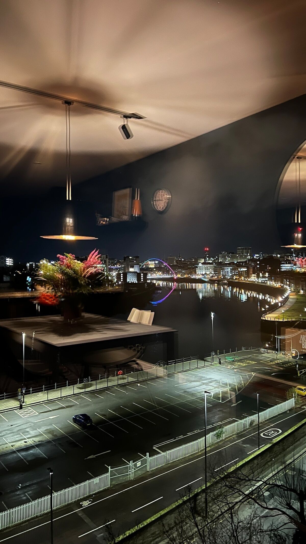 A modern building with a large glass facade overlooking a cityscape at night.