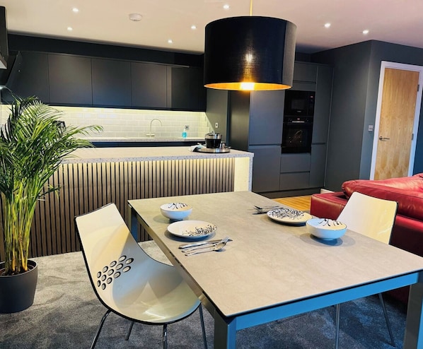 A modern kitchen with dark cabinets, a central island, and a dining area with a table and chairs.