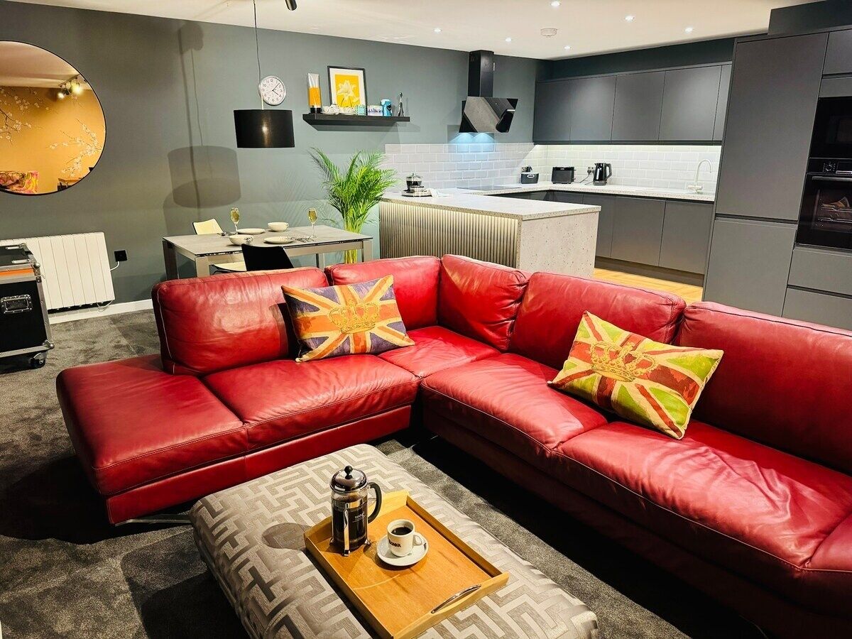 Ein modernes Wohnzimmer mit einem roten Ledersofa, einem Couchtisch mit Tablett und einer Küche im Hintergrund.