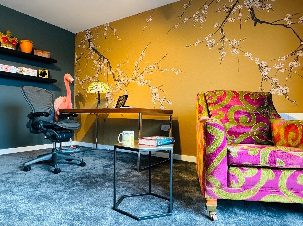 A room with a desk, chair, and colorful sofa.