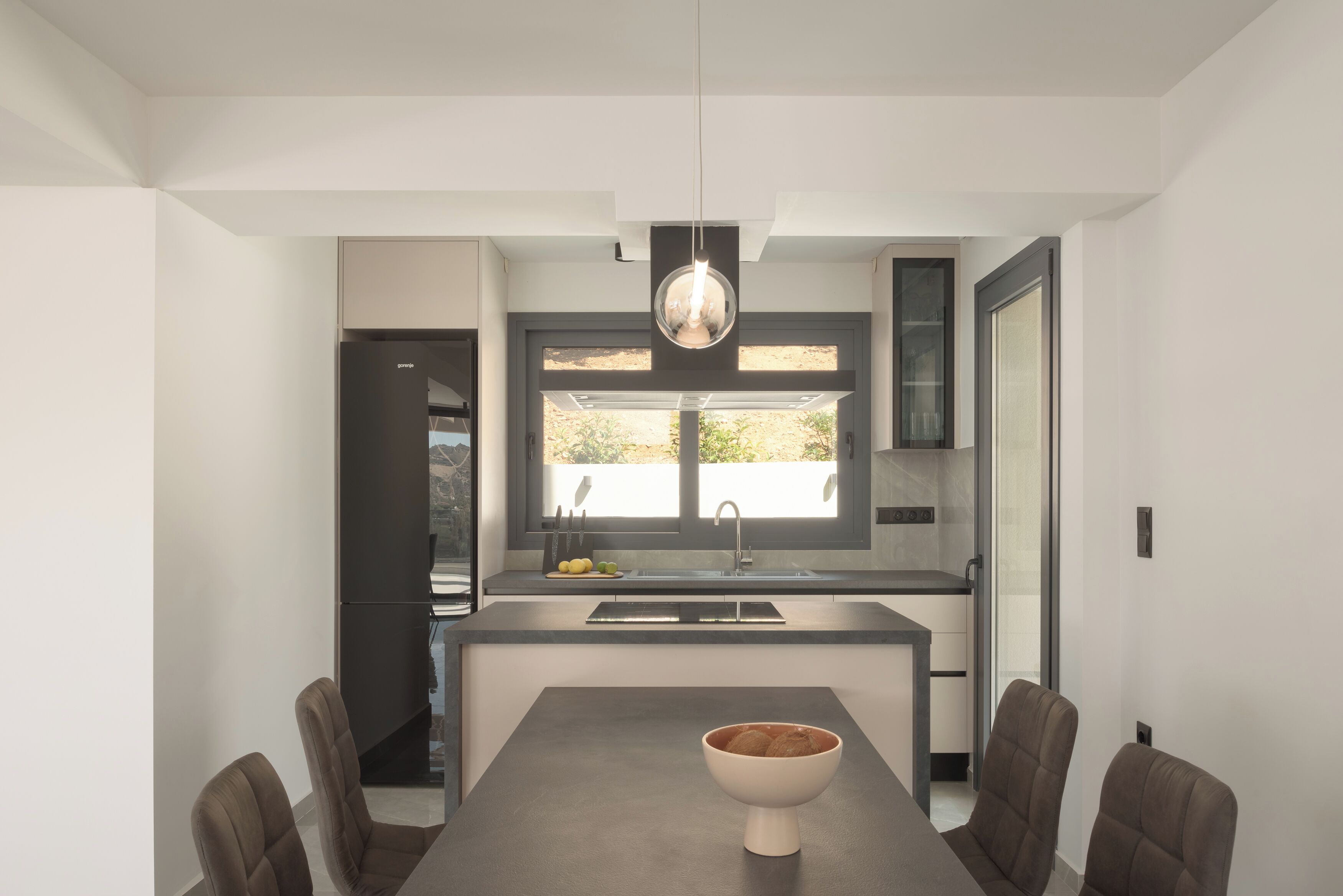 A modern kitchen with a central island, a dining area with a table and chairs, and a pendant light above.