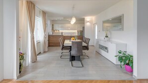 A modern kitchen with white cabinets, a dining area with a table and chairs, and a large mirror on the wall. - Evita Apartment - 60m to Beach, A/C in All Sleeping Areas! (Slatine)