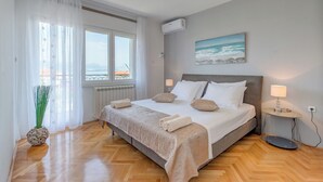 A neatly arranged bedroom with a large bed, a view of the sea through the window, and a wall-mounted air conditioner. - Evita Apartment - 60m to Beach, A/C in All Sleeping Areas! (Slatine)