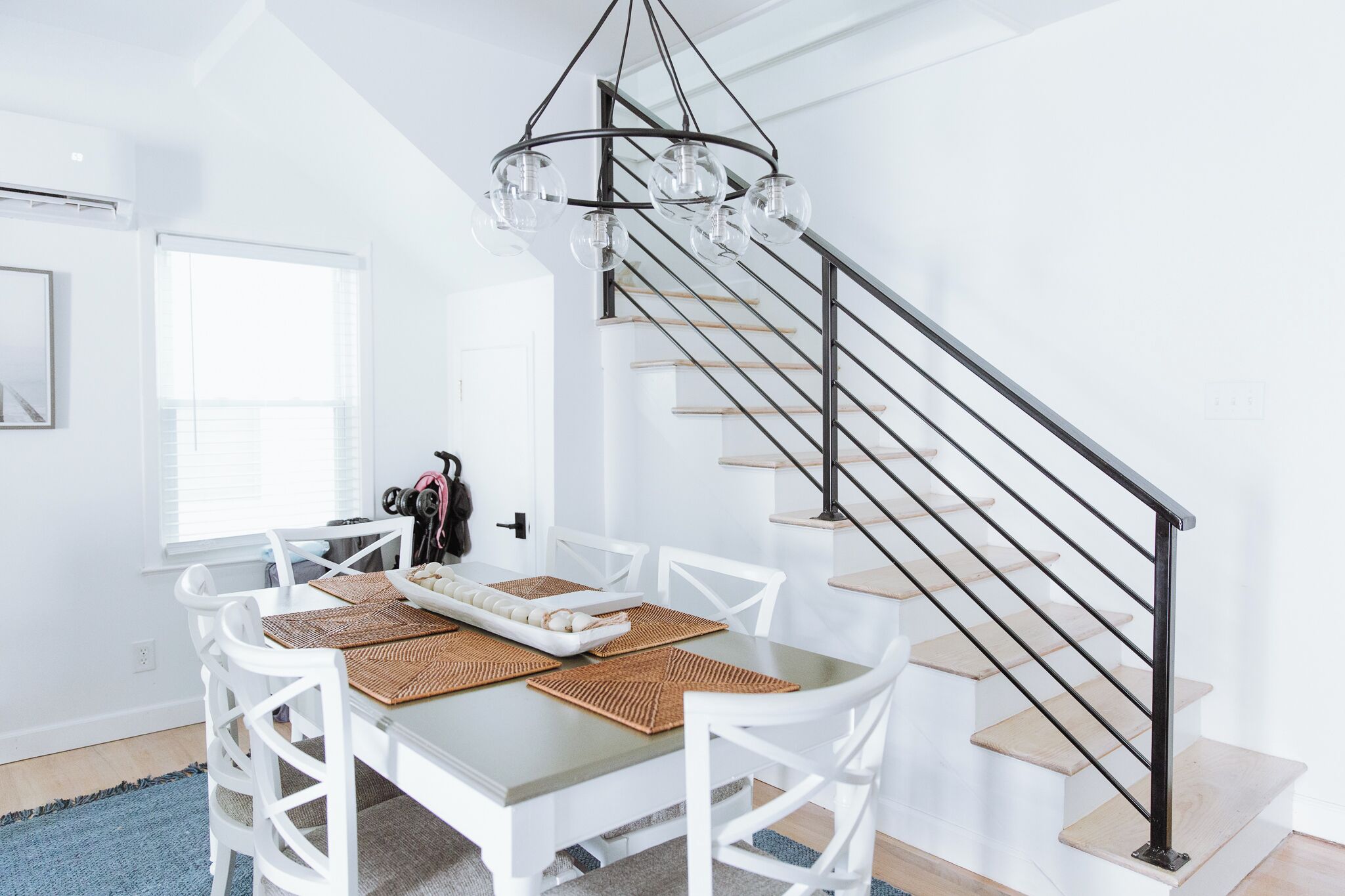 Un coin repas avec une table dressée pour quatre personnes, un escalier doté d’une rampe en métal et un luminaire suspendu.