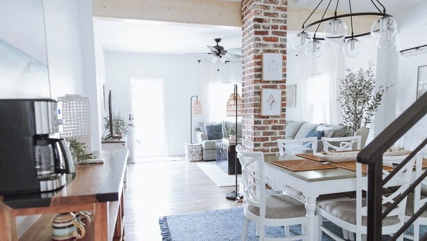 Uma cozinha moderna com parede de tijolos decorativa, armários brancos e uma área de jantar com mesa e cadeiras brancas.