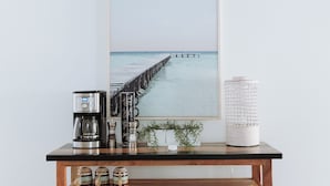Uma cafeteira, uma fotografia emoldurada de um cais e um objeto decorativo branco sobre uma mesa de madeira.