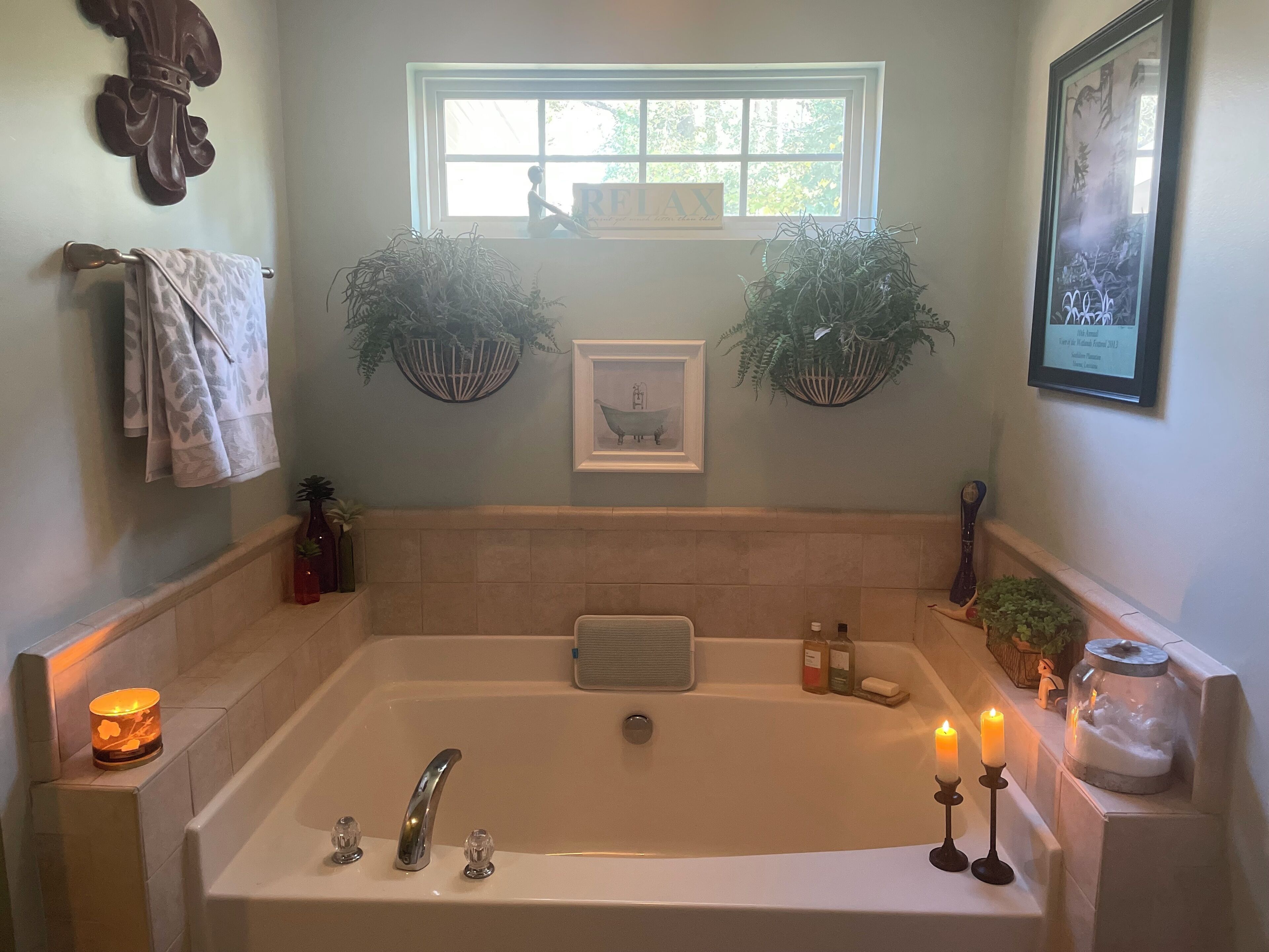 Ein Badezimmer mit einer großen Badewanne, einem Fenster, zwei Wandpflanzgefäßen, einem gerahmten Bild und einem Handtuchhalter.