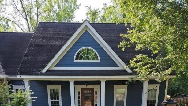 Une maison à deux étages avec un porche à l’avant, une porte d’entrée centrale et un petit jardin devant, agrémenté de parterres de fleurs.