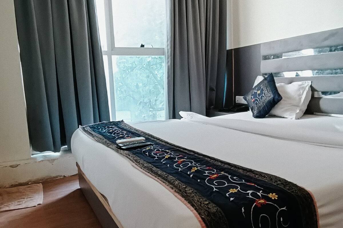 A hotel room with a large bed, a bedside table, a TV, and a window with curtains.