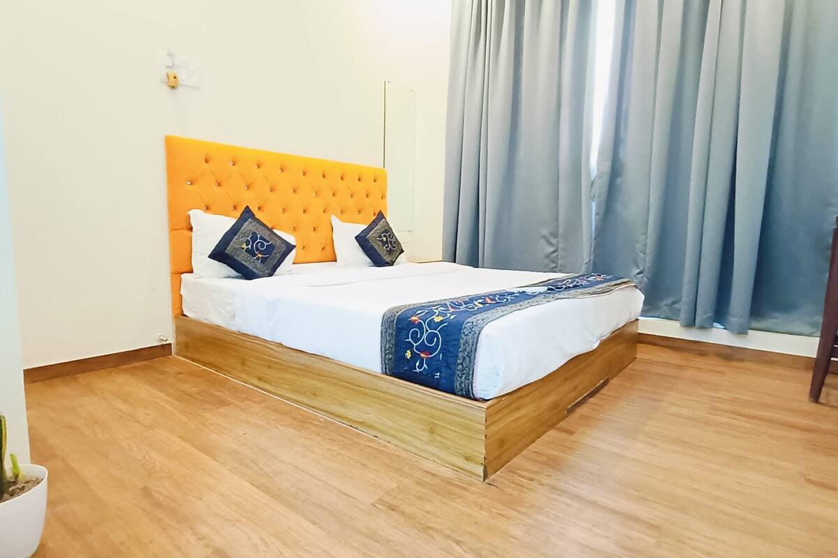A neatly made bed with a wooden frame and an orange headboard, accompanied by two decorative pillows.