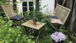 Ein kleiner Gartenbereich mit zwei Holzstühlen, einem Tisch und Topfpflanzen.