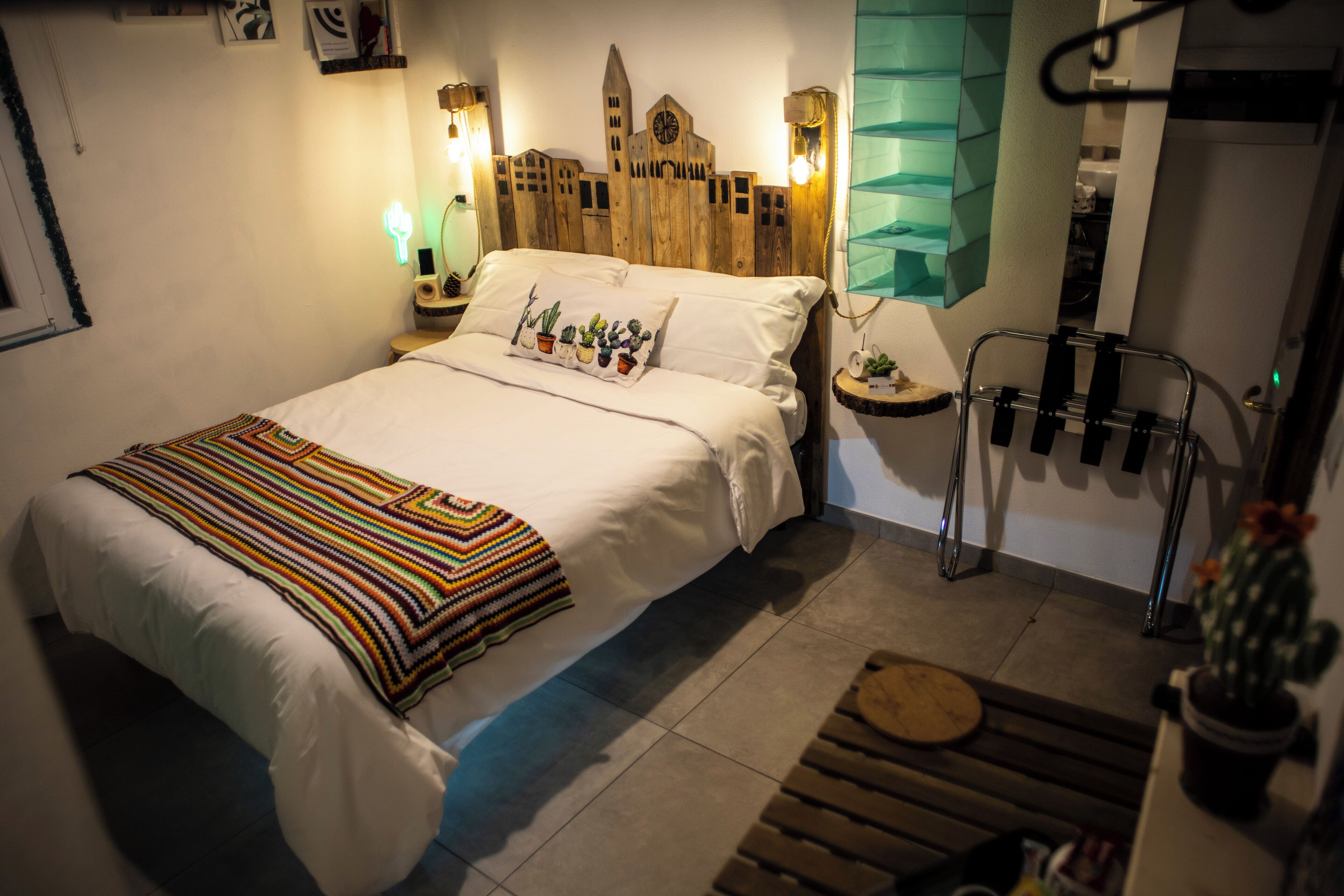 A neatly made bed with a striped blanket, a wooden headboard, and a wall-mounted clock.