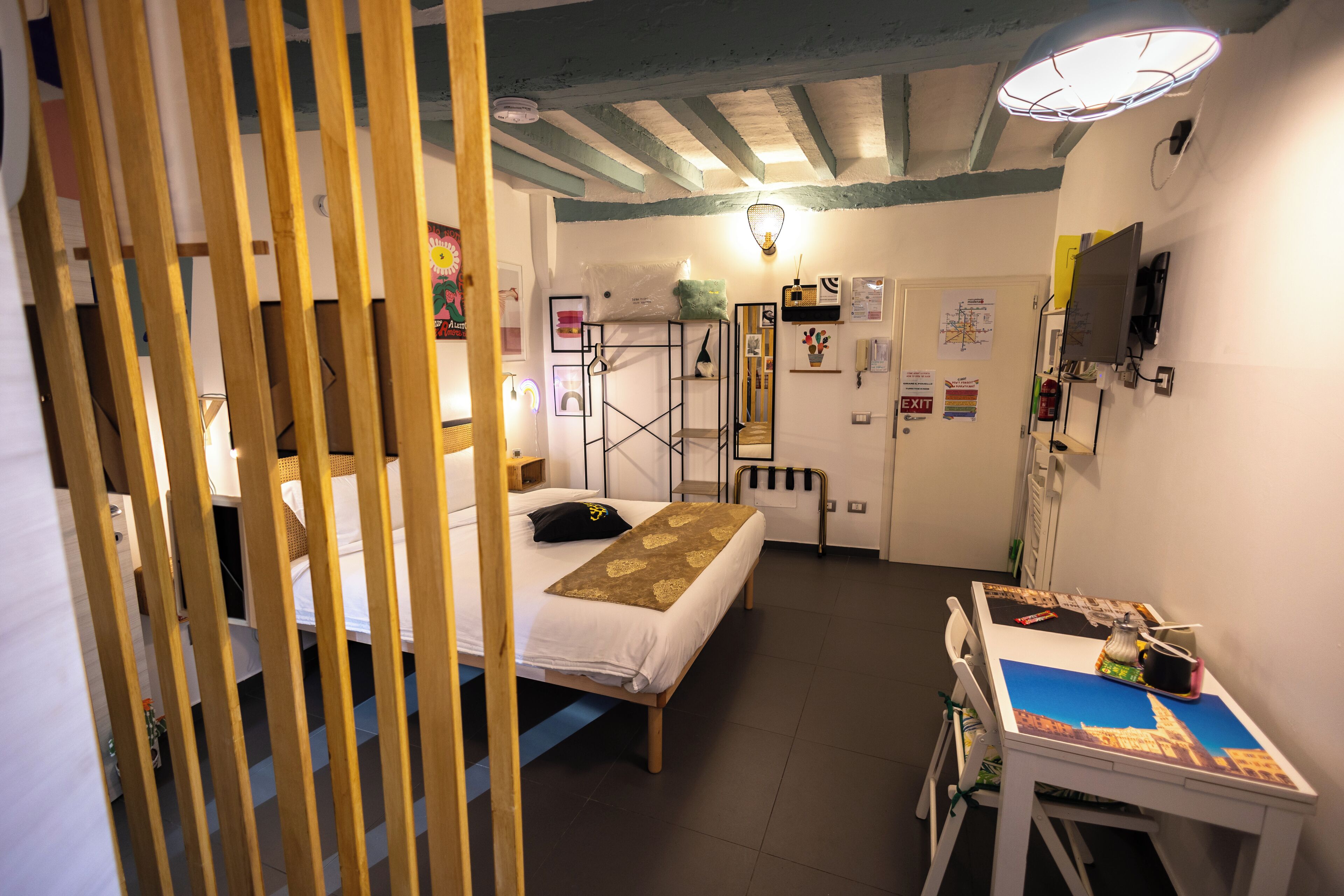 A room with a bed, a desk, and a chair. There is a map on the wall and a fire extinguisher.
