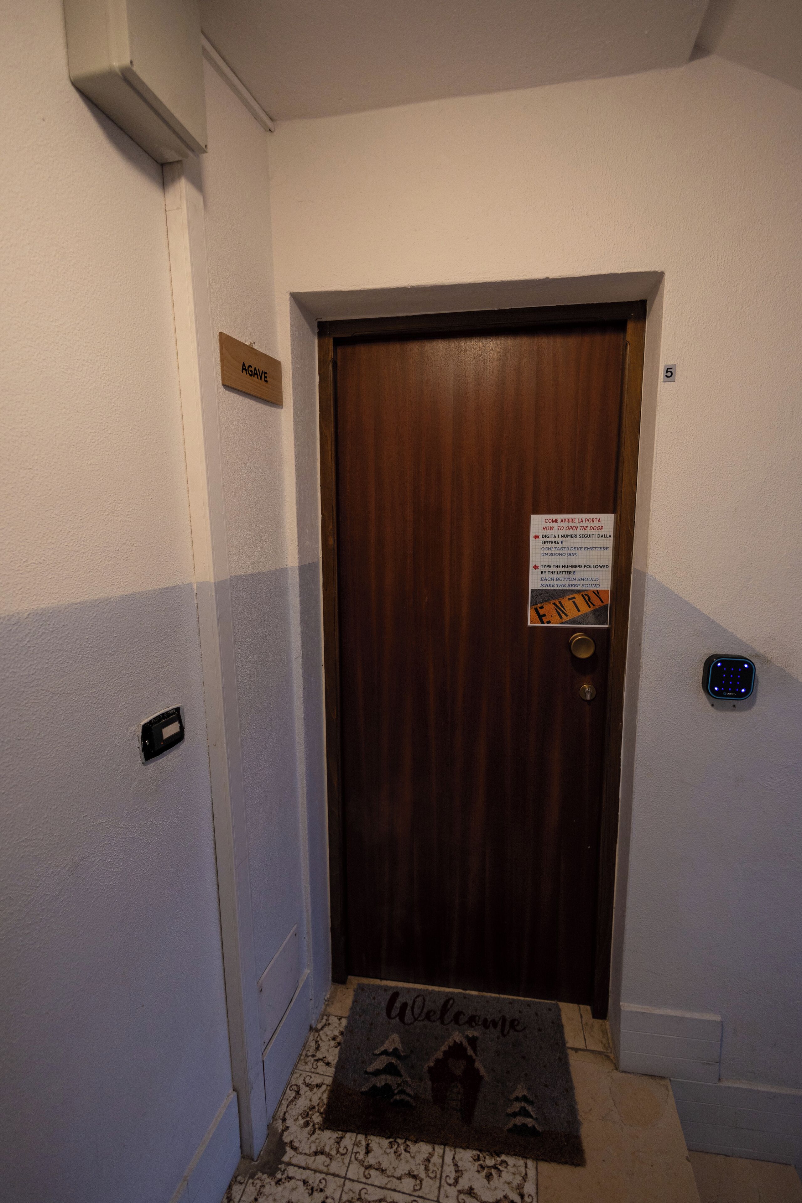 A hotel entrance with a wooden door, a welcome mat, a sign indicating room number 5, and a digital keypad.
