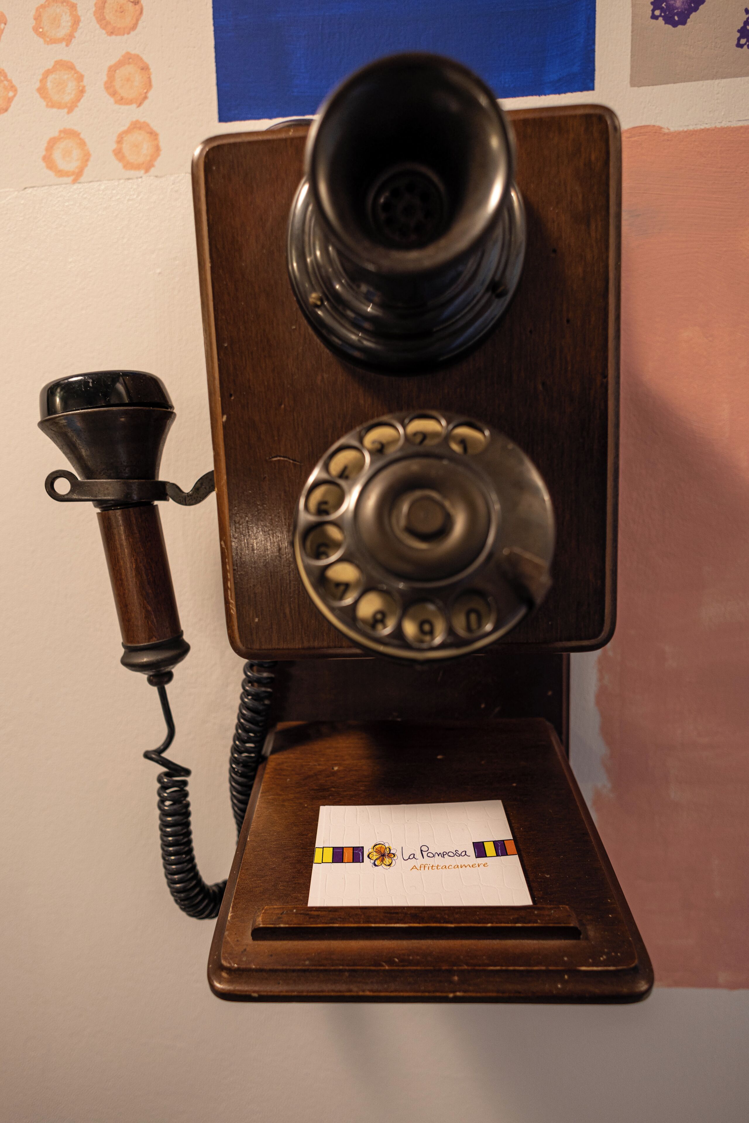 A vintage rotary dial telephone with a wooden base, mounted on a wall.