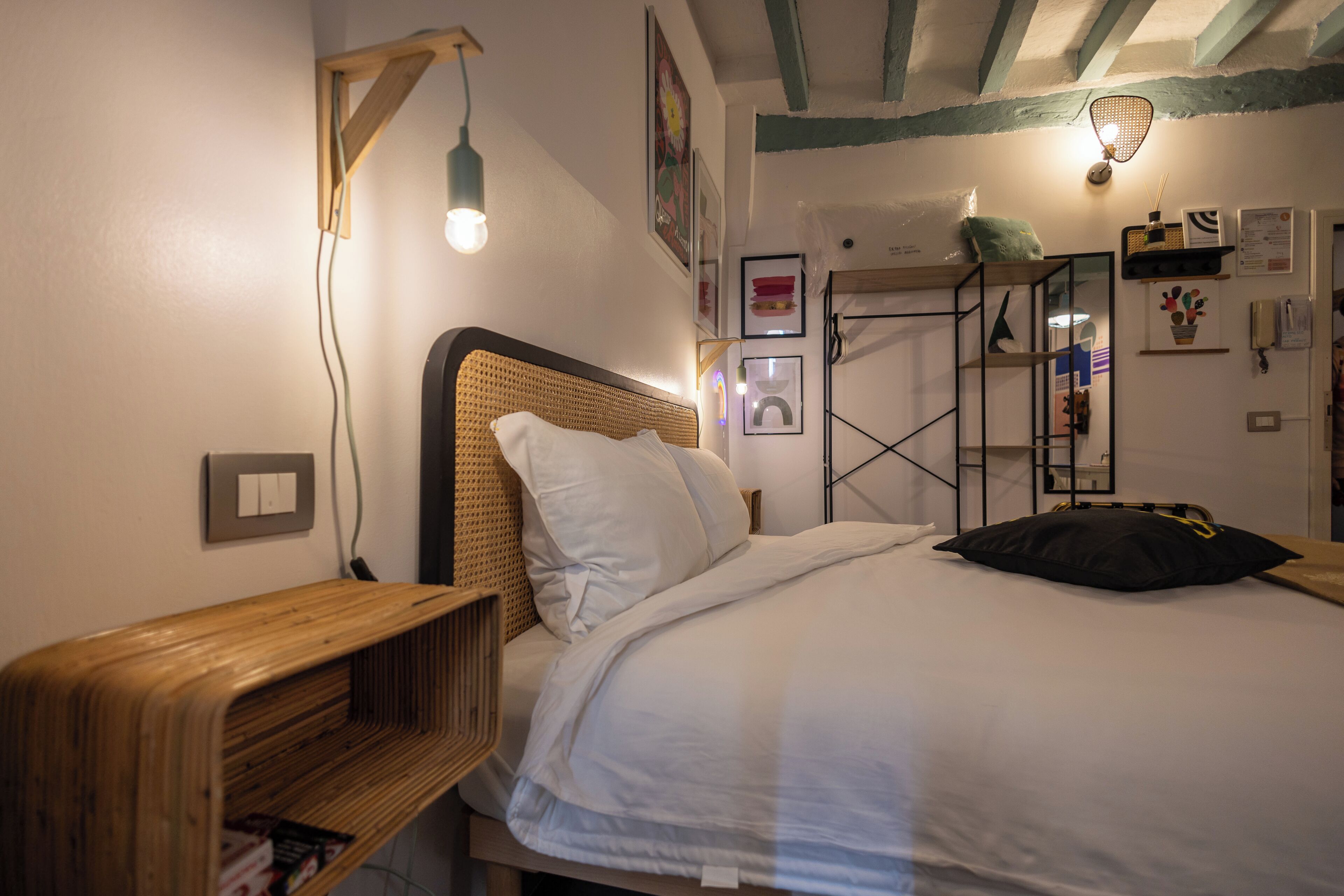 Ein Schlafzimmer mit einem Holzkopfteil, einem Bett mit weißer Bettwäsche, einem Nachttisch aus Holz und einem Wandregal.