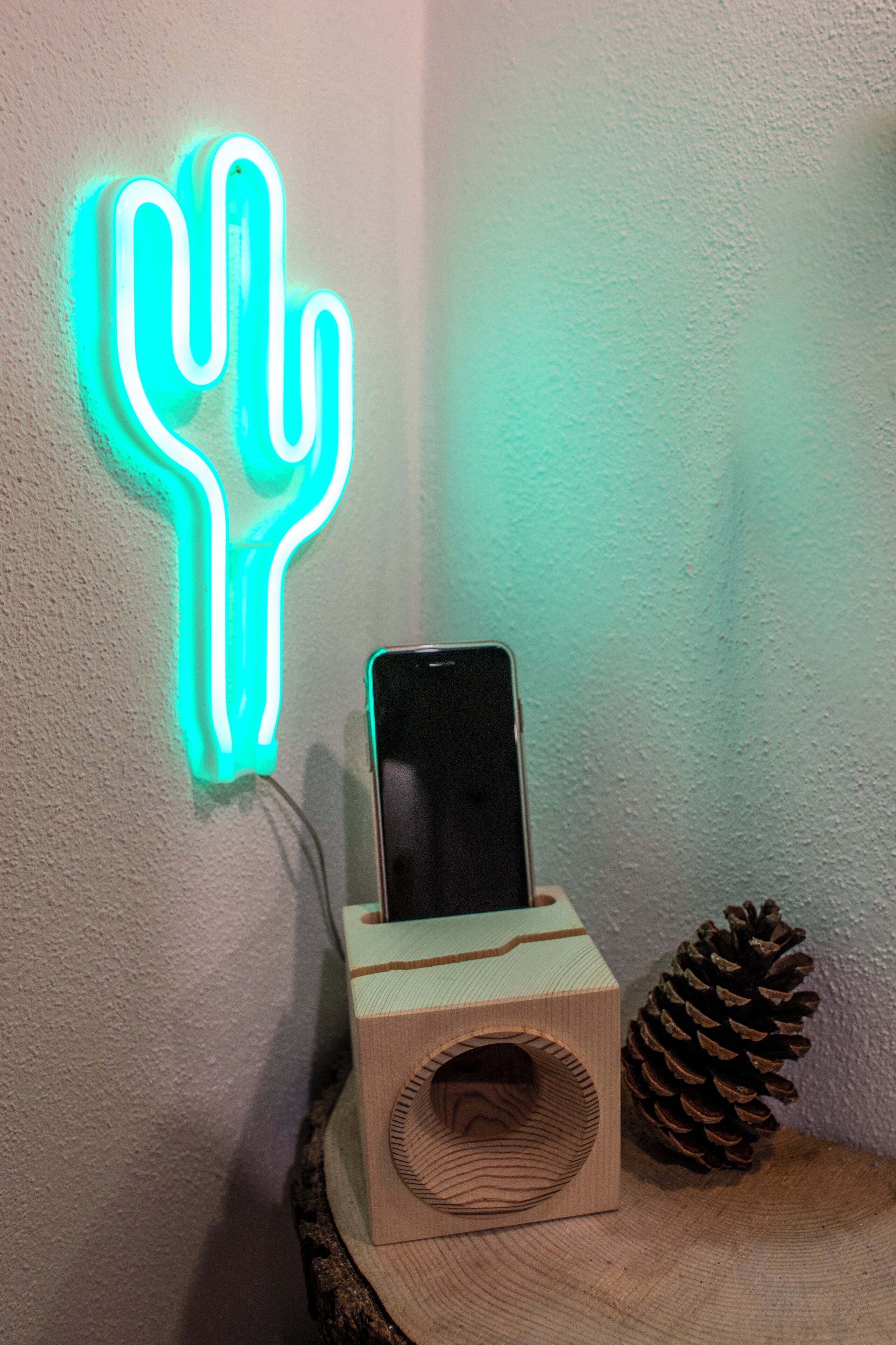 Un teléfono inteligente cargándose sobre un soporte de madera, con una luz de neón con forma de cactus al fondo.