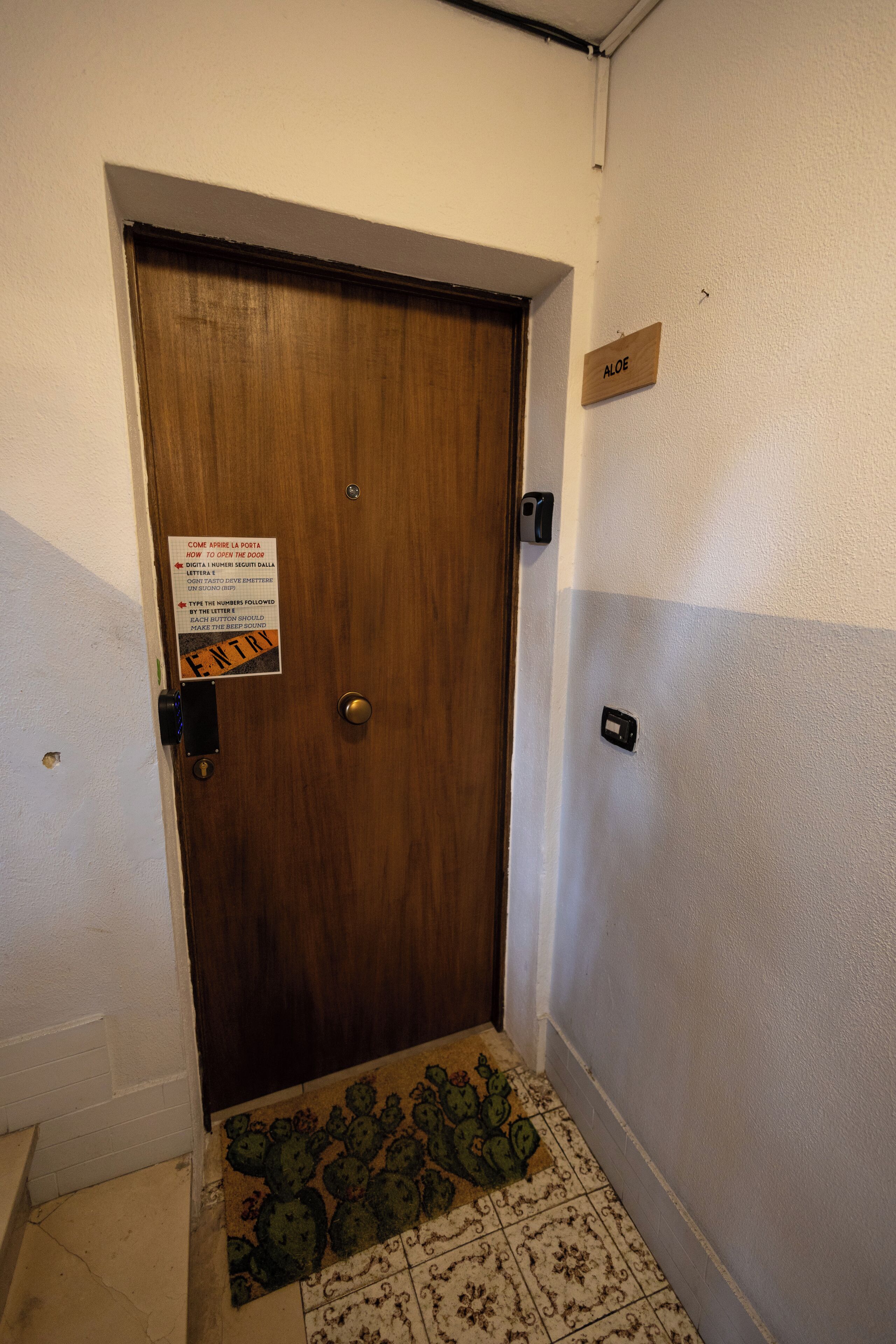 A wooden door with a sign indicating an entry point, a nameplate above it, and a patterned floor.