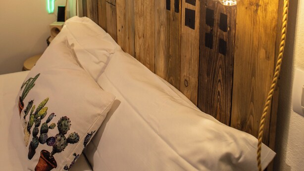 Una cama con un almohadón blanco, un cabecero de madera y una lámpara colgante.