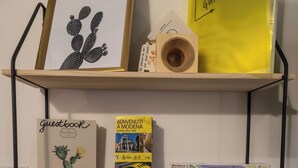 Una estantería con una obra de arte de cactus enmarcados, un libro de visitas, una guía para huéspedes, un carrete de madera, un mapa turístico y un control remoto.