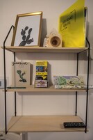 Hyllyllä on kehystetty kaktusta kuvaava taideteos, vieraskirja, opas, puinen lankkarulla, matkailukartta ja kaukosäädin.