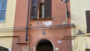 Un edificio con una puerta marrón, una ventana pequeña con persianas y una farola.