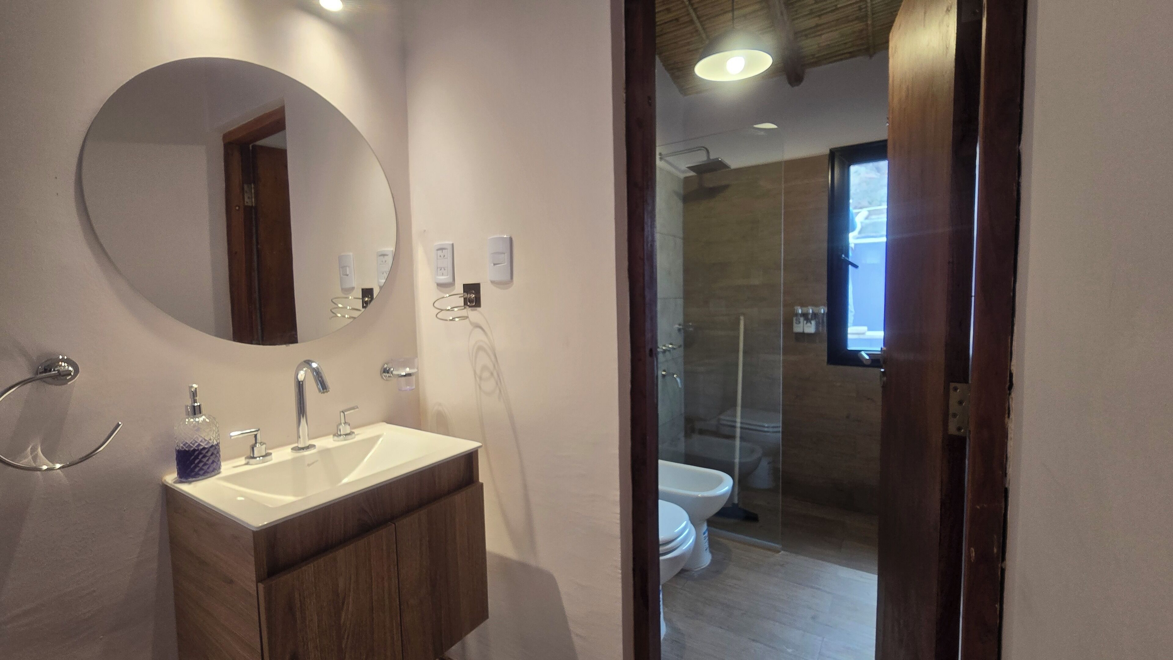 A modern bathroom with a round mirror, a white sink, and a glass shower enclosure.