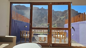 A room with a sliding glass door leading to an outdoor patio with a table and chairs, a view of mountains, and a wooden fence. - El cielo en Tilcara complejo turístico (Tilcara)