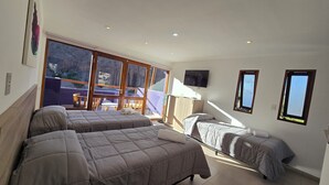 A hotel room with two beds, a balcony with a table and chairs, and a TV mounted on the wall. - El cielo en Tilcara complejo turístico (Tilcara)